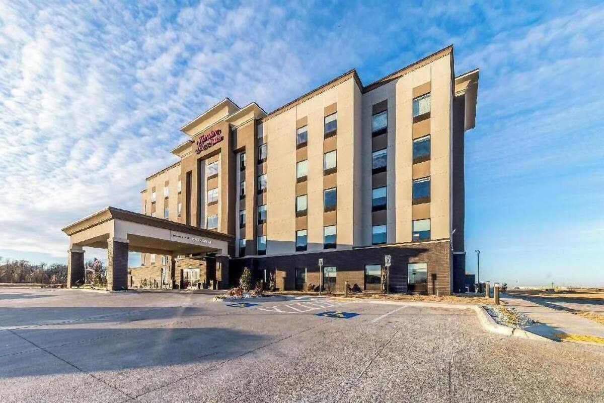 A multi-story hotel with a covered entrance, a parking lot, and a clear sky.