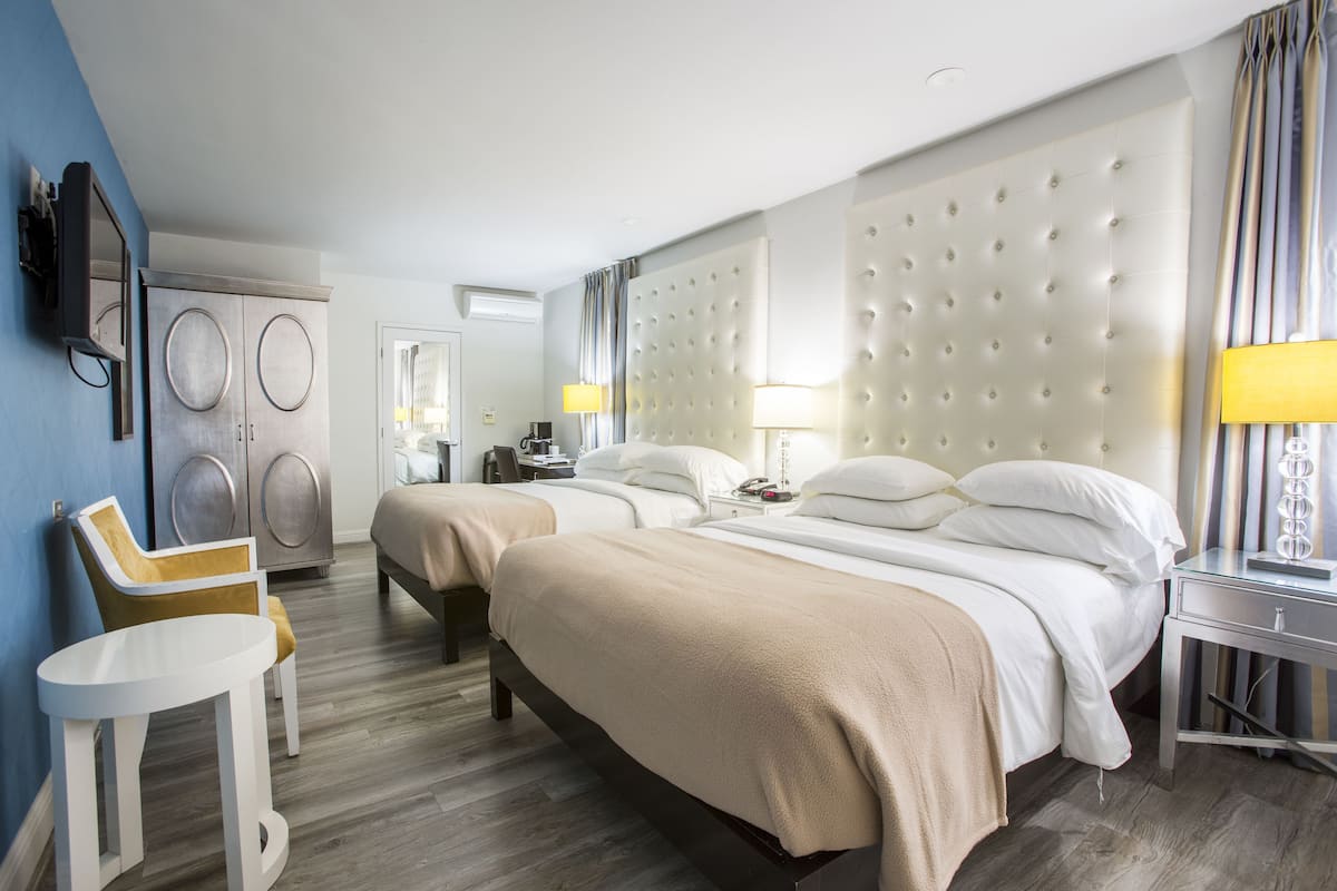 A hotel room with two beds, a small table, a chair, a wardrobe, and a television.