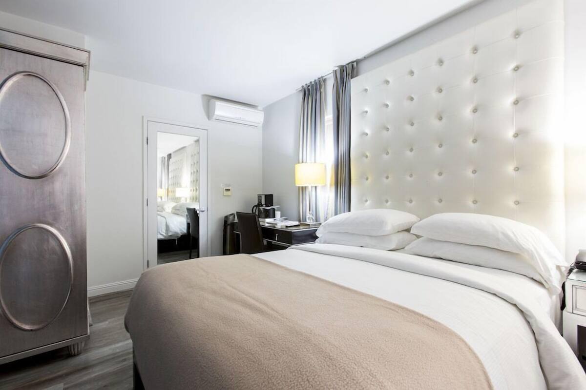A hotel room with a large bed, a desk, a wardrobe, and a mirror.