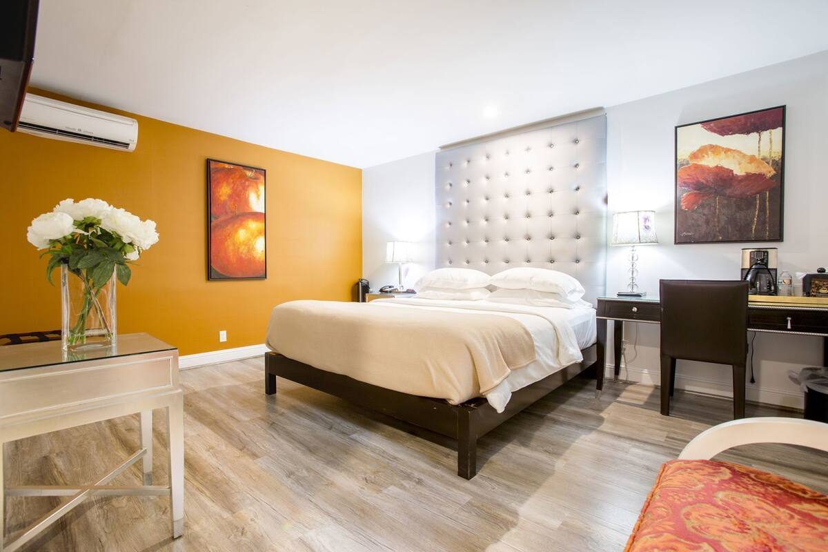 A hotel room with a bed, bedside table, desk, chair, and artwork on the walls.