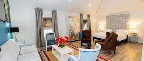 Una habitación de hotel moderna con sofá, sillón, mesa de centro y una cama con cabecero.