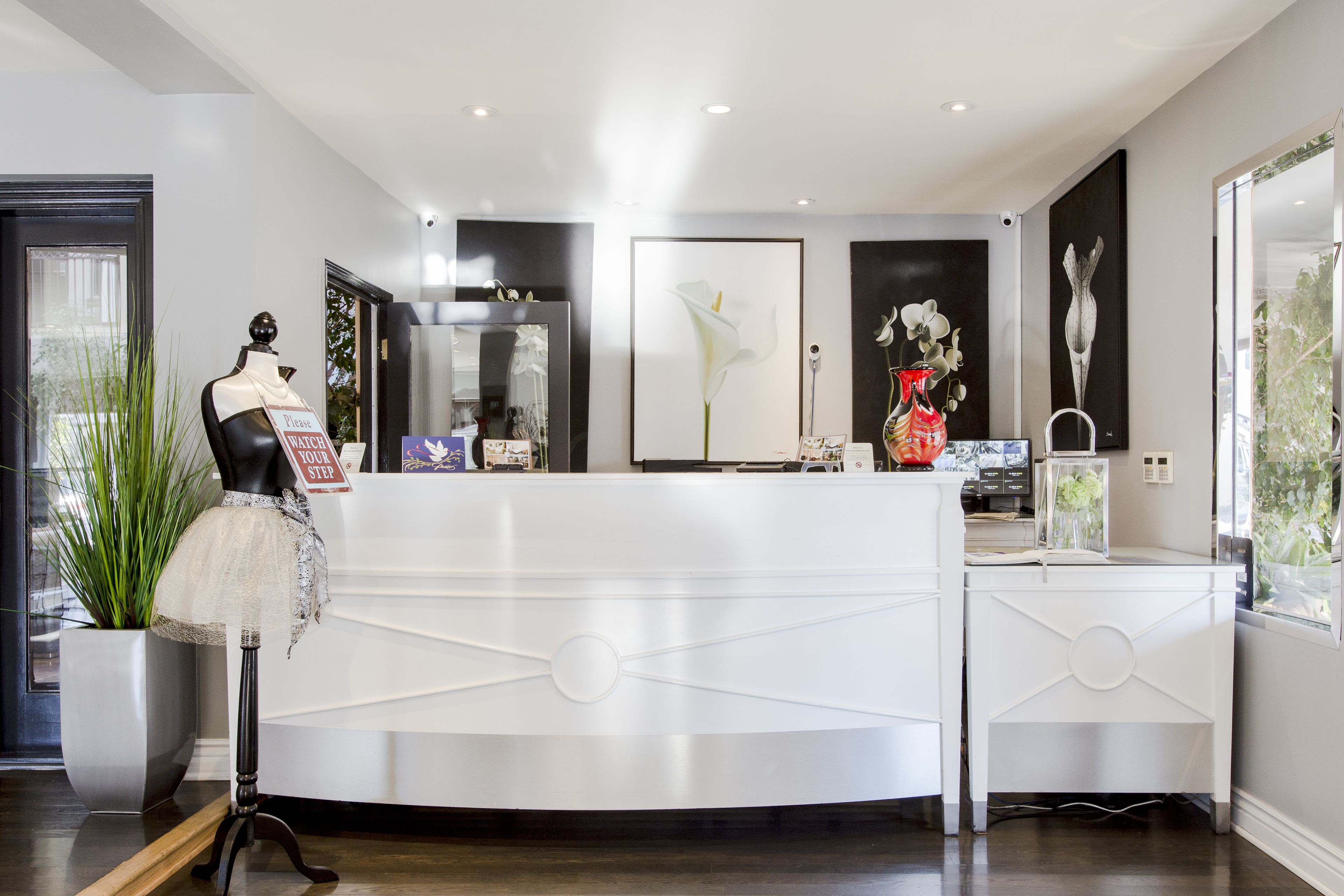 A modern reception desk with a white design, a mannequin dressed in a tutu, and a potted plant.