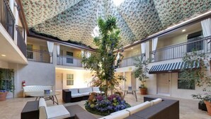 Ein großzügiger Innenhof mit einem zentralen Garten, verschiedenen Sitzbereichen und einer hohen Decke mit Musterdesign.