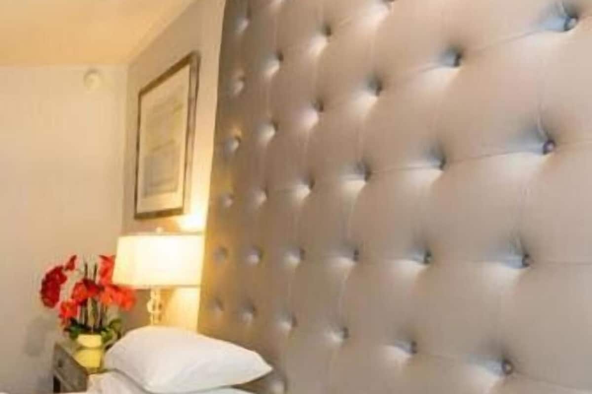 A hotel room with a tufted headboard, a bed with white linens, a nightstand with a lamp and a vase of flowers.