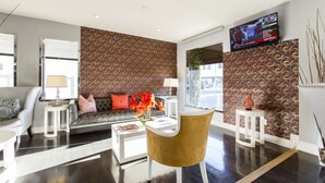 Ein modernes Wohnzimmer mit einem Wandpapier mit Muster, einer Couch mit Kissen, einem Couchtisch, einem an der Wand montierten Fernseher und einer Vase mit Blumen.