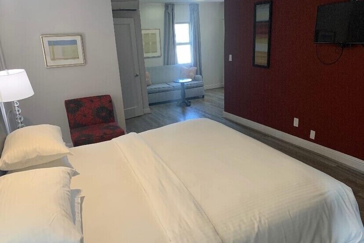 A hotel room with a large bed, a chair, a desk, and a window with curtains.