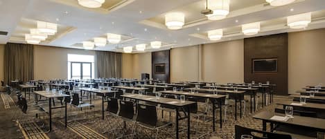 Une salle de conférence dotée de plusieurs tables et chaises, de grandes fenêtres et d’un tapis à motifs.