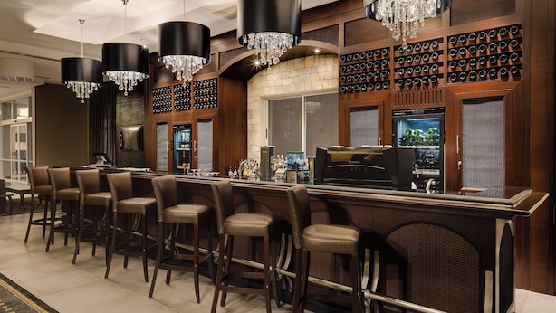 A bar area with a long counter, multiple bar stools, and a wine rack. - Protea Hotel Owerri Select (Owerri)