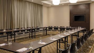 Un salón de conferencias con mesas largas, sillas y una pantalla grande en la pared.