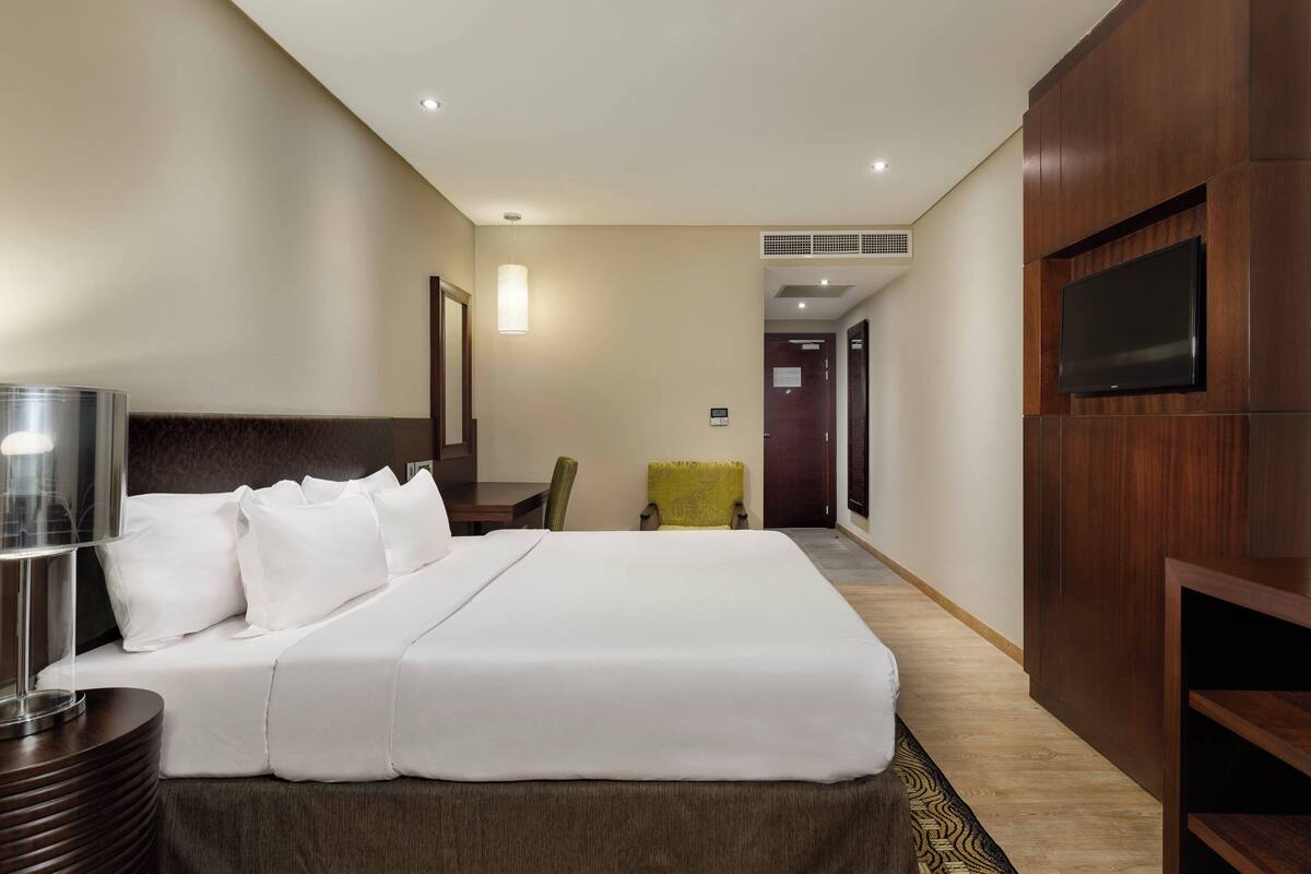 A hotel room with a large bed, a bedside table, a TV mounted on the wall, and a chair.