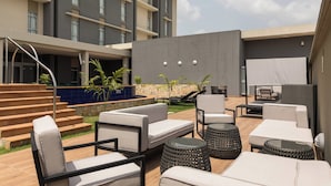 An outdoor seating area with multiple sofas and round tables, a pool, and a staircase leading to an upper level. - Protea Hotel Owerri Select (Owerri)