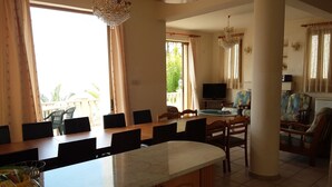 Un comedor amplio con una larga mesa de madera y sillas, un televisor y vistas al exterior.
