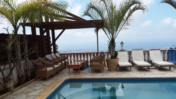 Un área de piscina con sillones de descanso y una pérgola, rodeada de plantas en macetas.