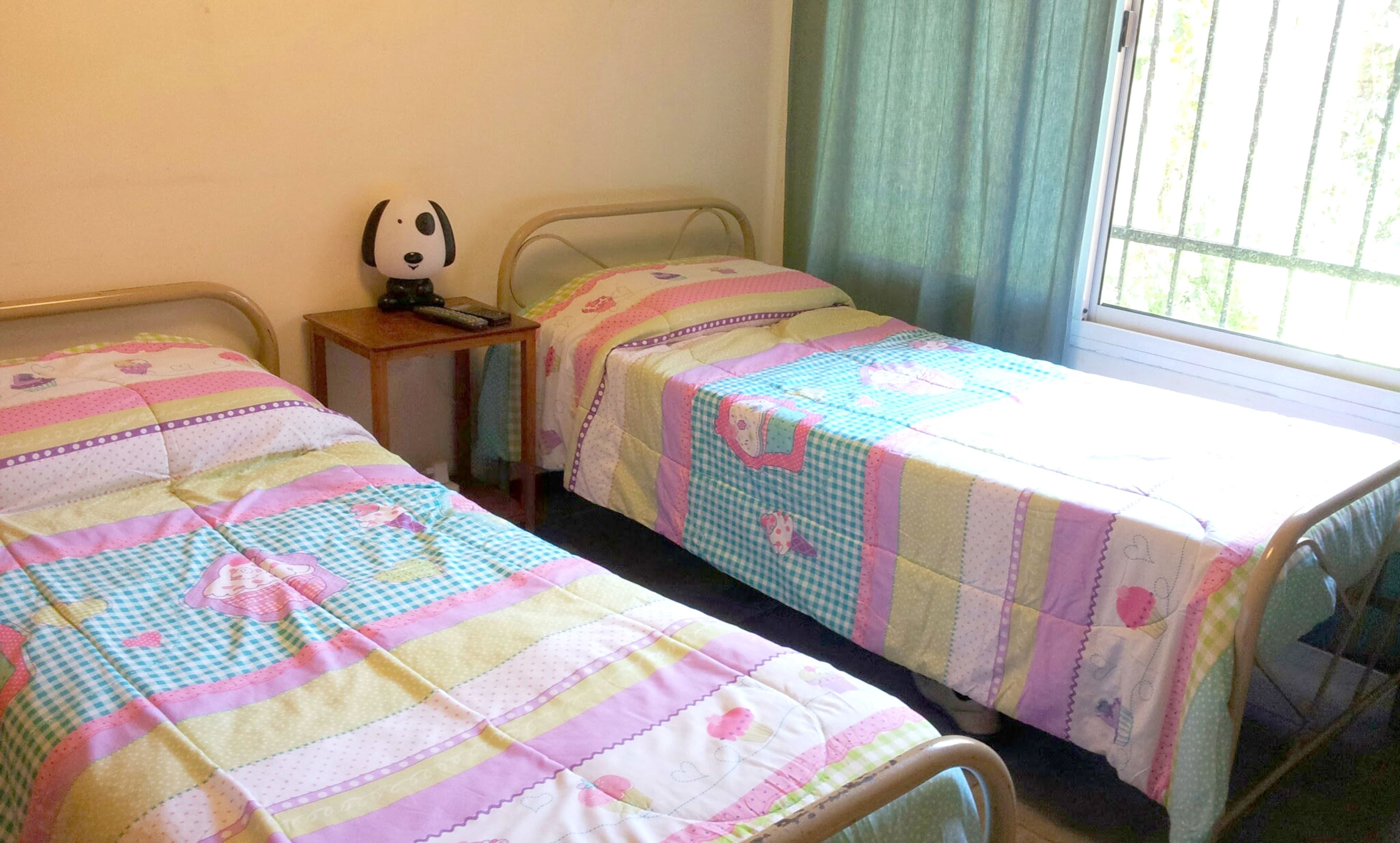 Una habitación con dos camas individuales, una mesita de noche con control remoto y una ventana con cortinas.