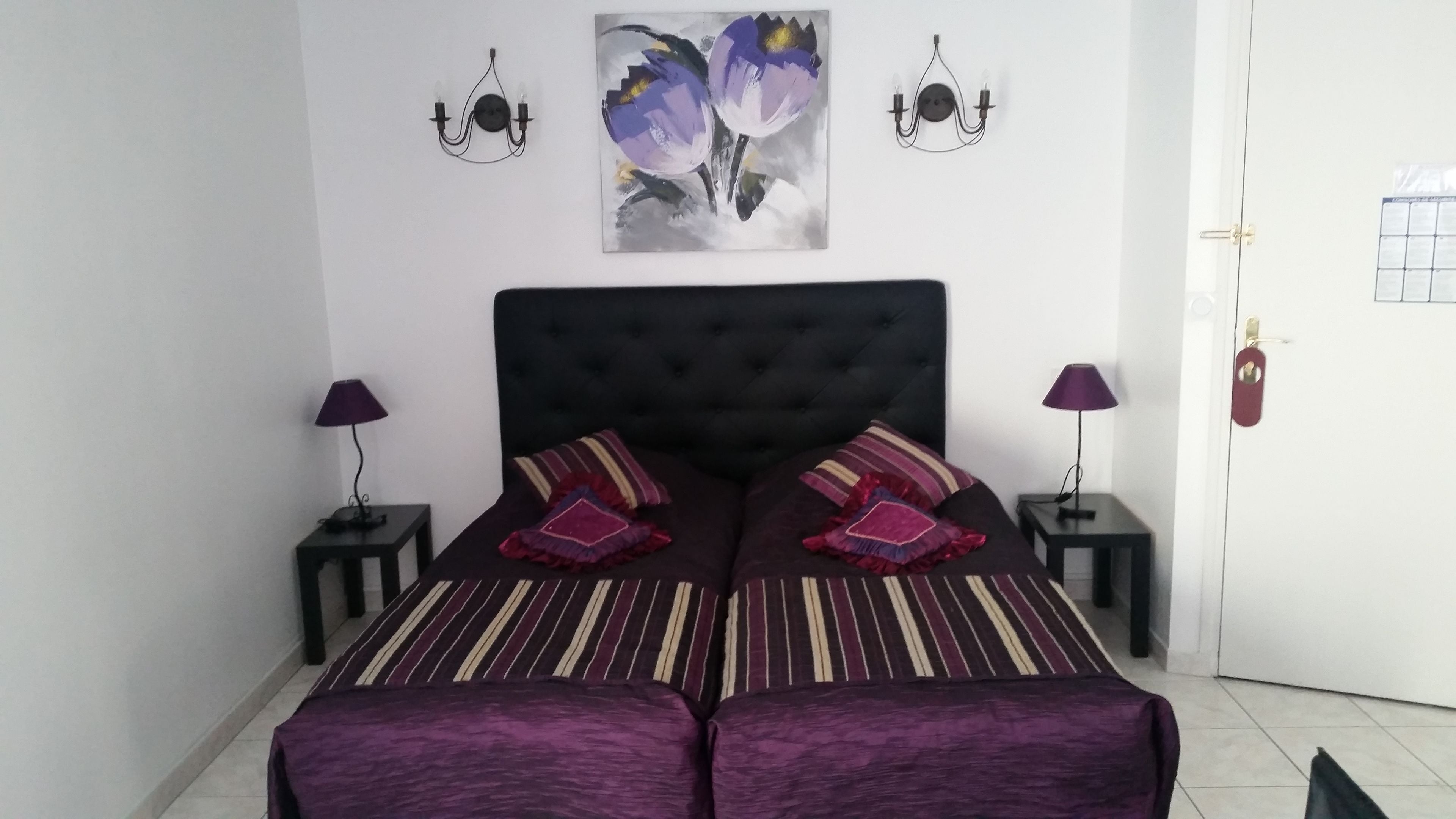 Un dormitorio con una cama grande, dos mesitas de noche, dos lámparas de pared y un cuadro sobre la cama.