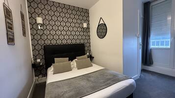 A neatly made bed with a grey blanket, a headboard, and two bedside lamps.