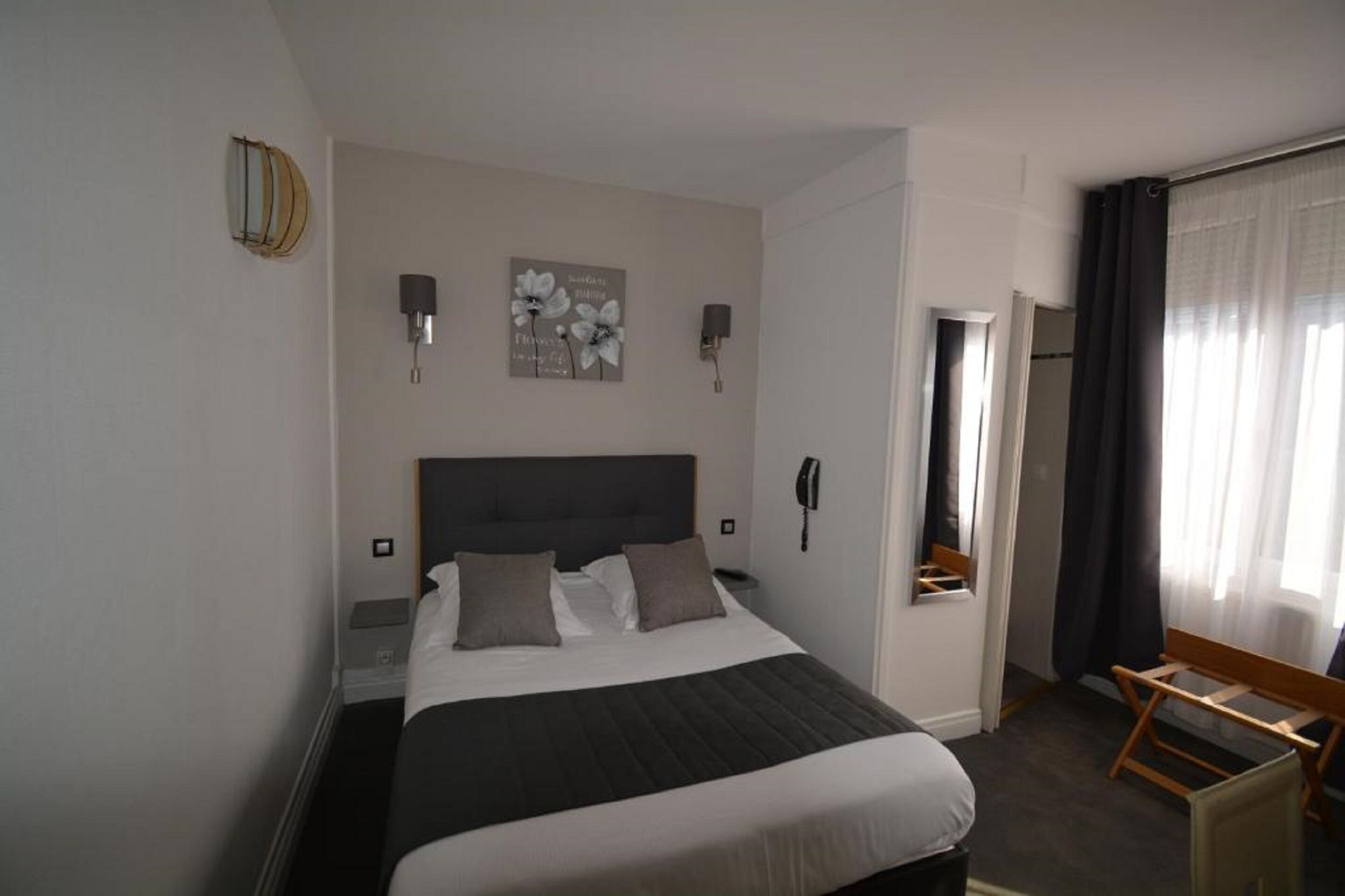 A hotel room with a large bed, bedside lamps, a bedside phone, a small table, and a window with curtains.