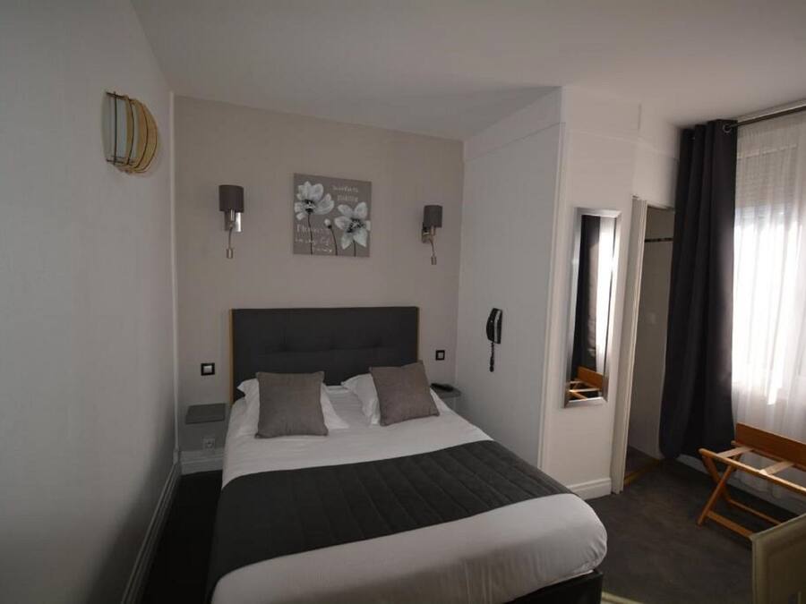 A hotel room with a large bed, bedside lamps, a bedside phone, a small table, and a window with curtains.