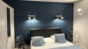 A bedroom with a geometric-patterned wall, a bed with patterned bedding, a chair, and a wardrobe.