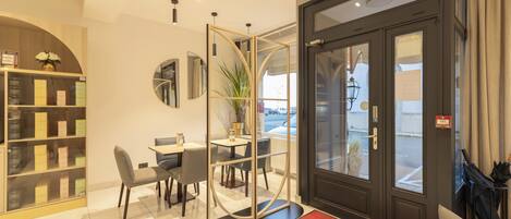 A hotel reception area with a reception desk, seating, a glass door entrance, and a red carpet with a logo.