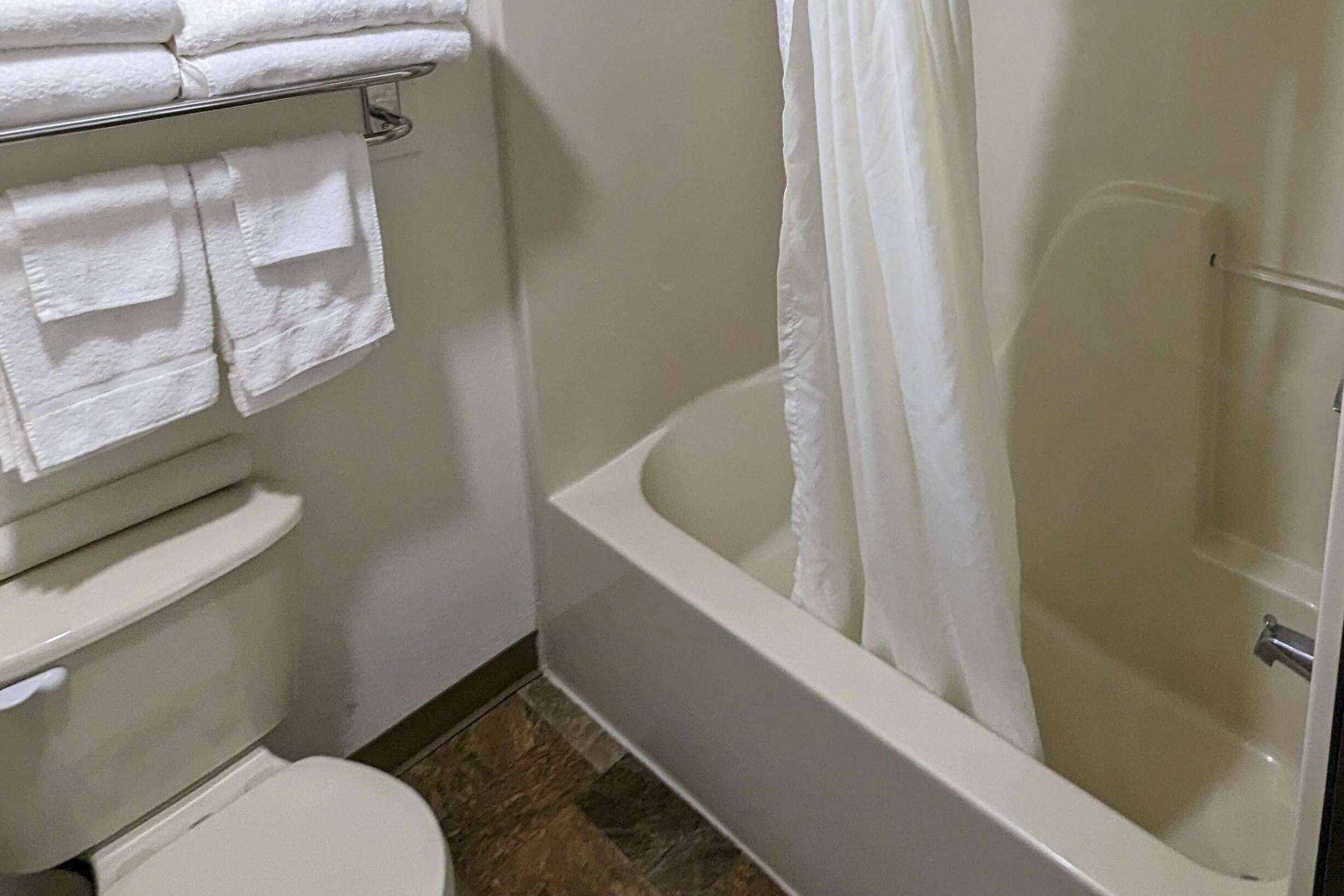 A bathroom with a bathtub, toilet, and a towel rack with folded towels.