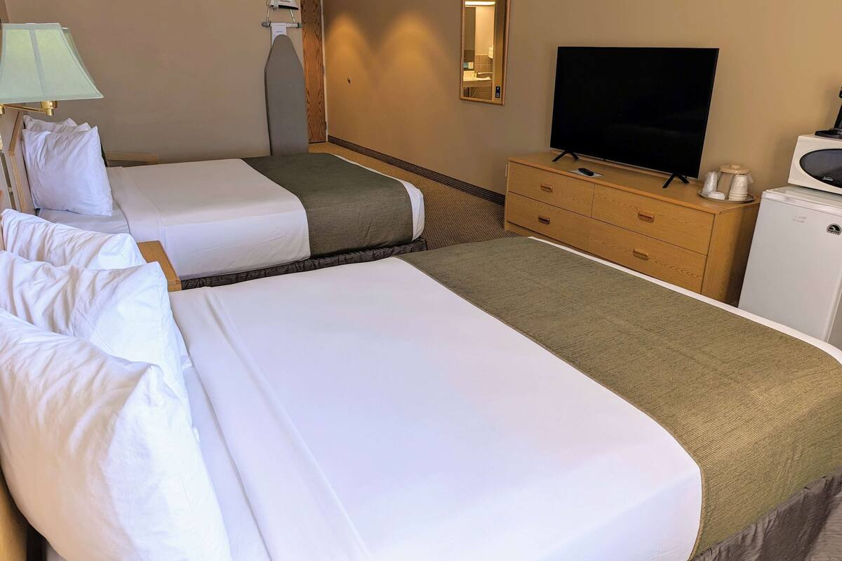 A hotel room with two beds, a TV, a dresser, and a microwave.