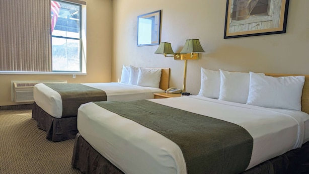 Una habitación de hotel con dos camas, una mesita de noche, una lámpara y una ventana con persianas.