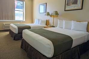 Una habitación de hotel con dos camas, una mesita de noche, una lámpara y una ventana con persianas.