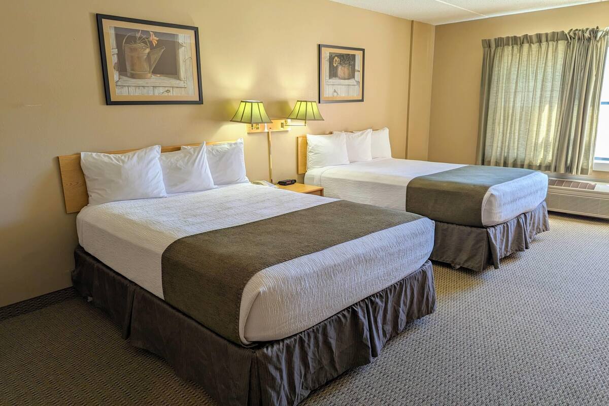 A hotel room with two beds, a nightstand, lamps, and framed artwork on the walls.