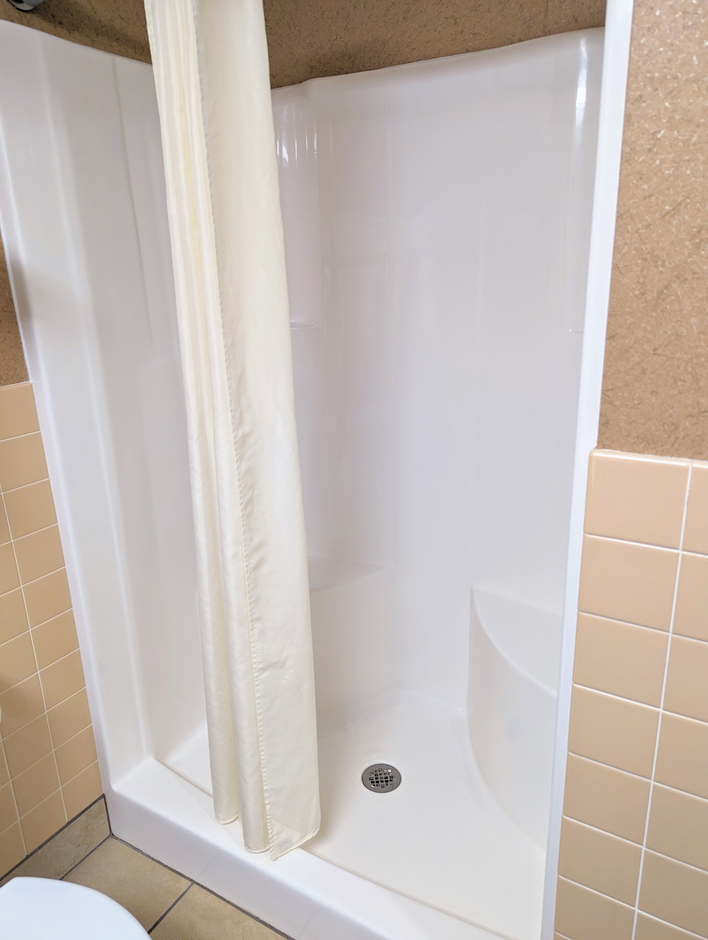 A white bathtub with a shower curtain, beige tiled walls, and a visible drain.
