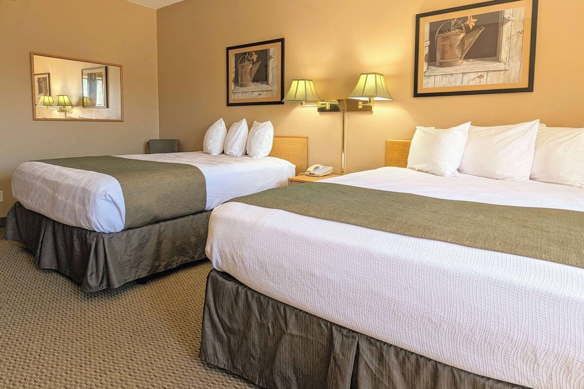 A hotel room with two beds, a nightstand, a lamp, and a framed picture on the wall.