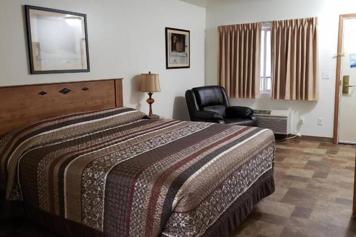 A bedroom with a bed, a chair, a lamp, a picture on the wall, and a window with curtains.