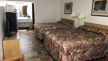 Habitación de hotel con dos camas, televisión, escritorio y baño visible a través de una puerta abierta.