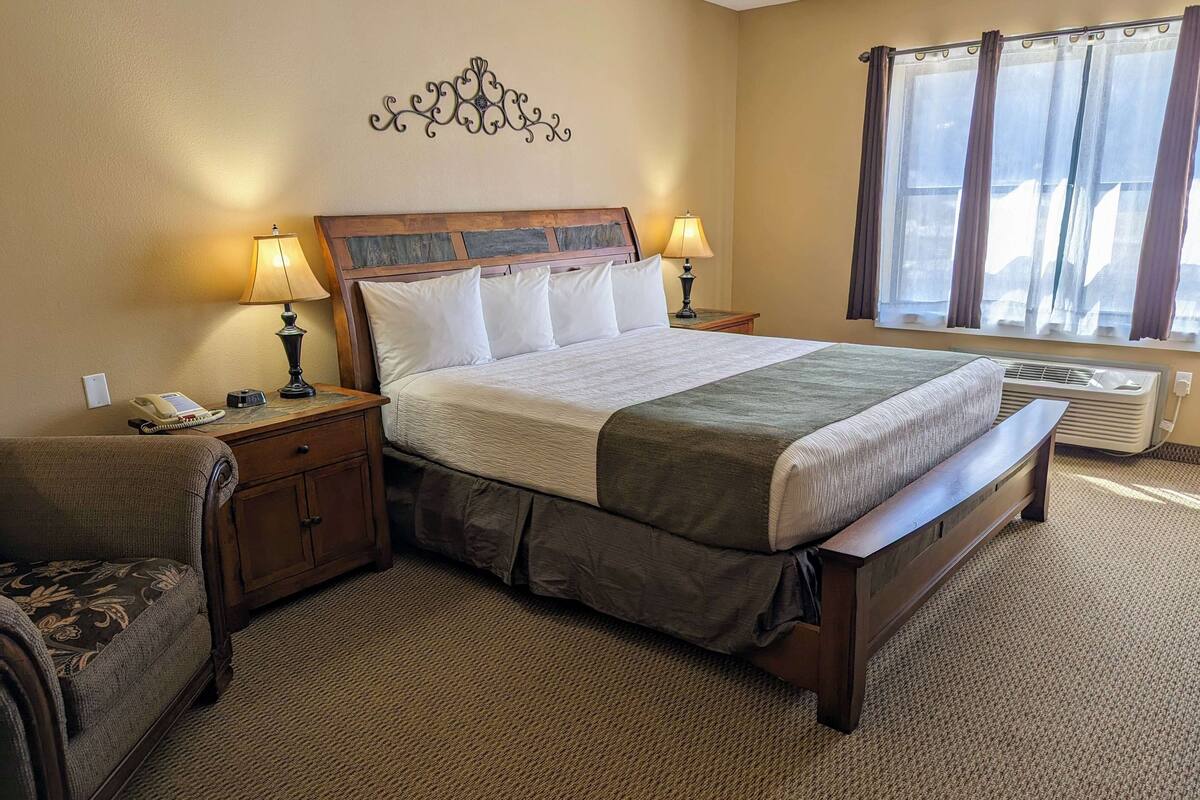 A neatly arranged hotel room with a large bed, two bedside tables with lamps, a small sofa, and a decorative wall piece.