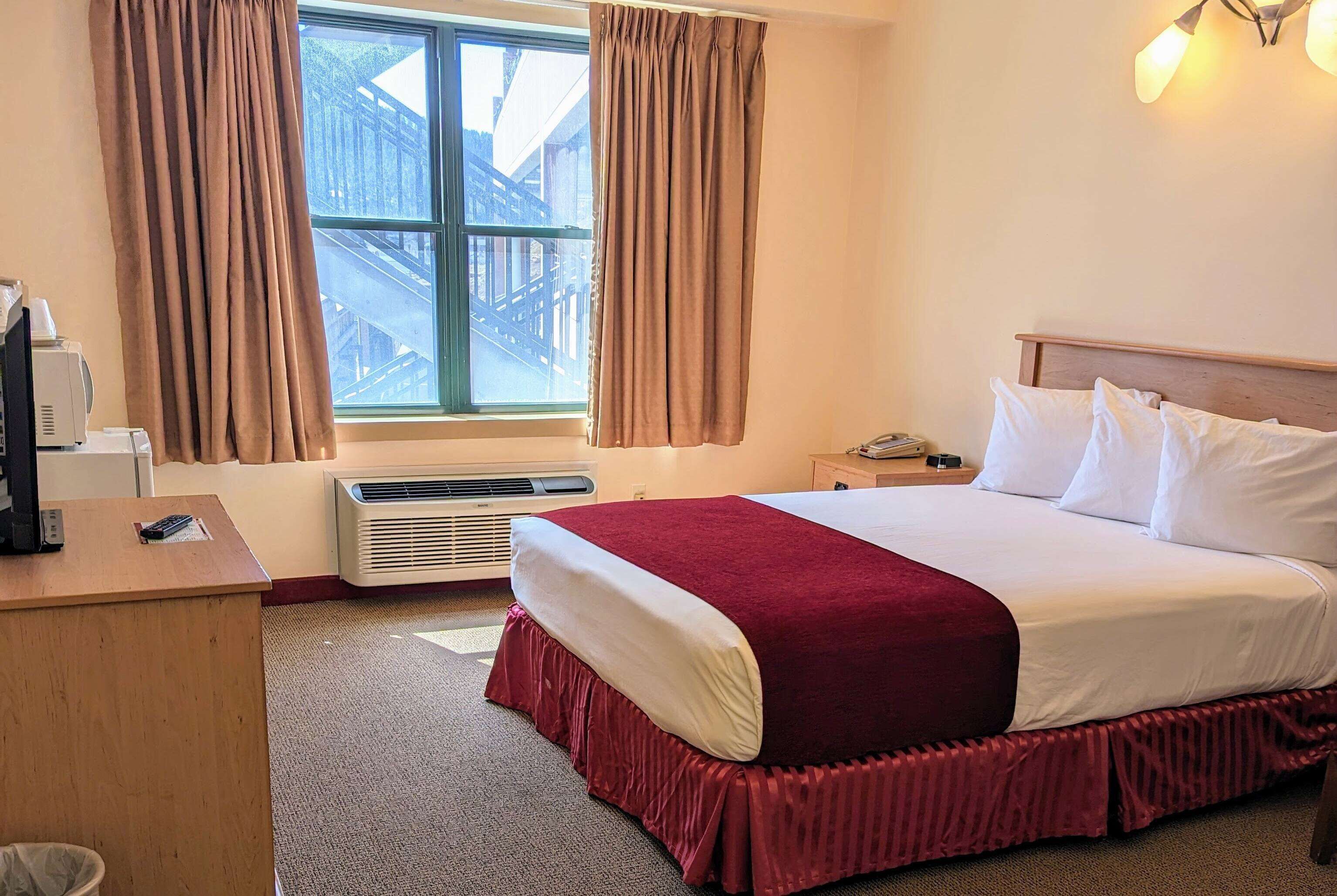 Una camera d'albergo con un letto, una scrivania, un telefono e una finestra con tende.