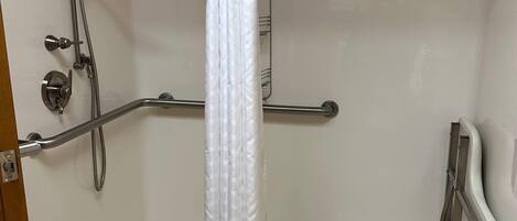 A shower area with a white shower curtain, grab bars, and a handheld showerhead.