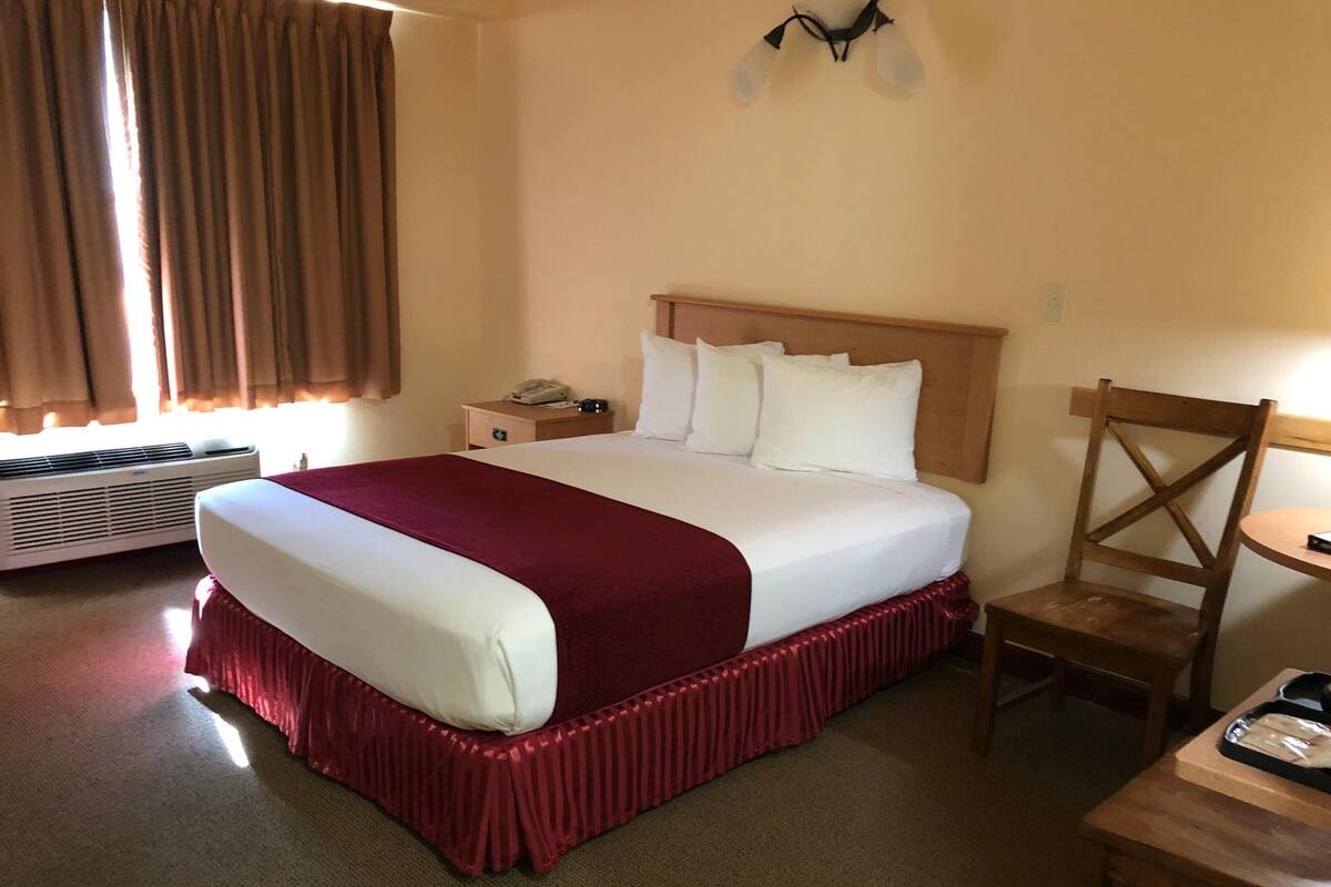 A hotel room with a large bed, a wooden nightstand, a chair, and a table with a tray.