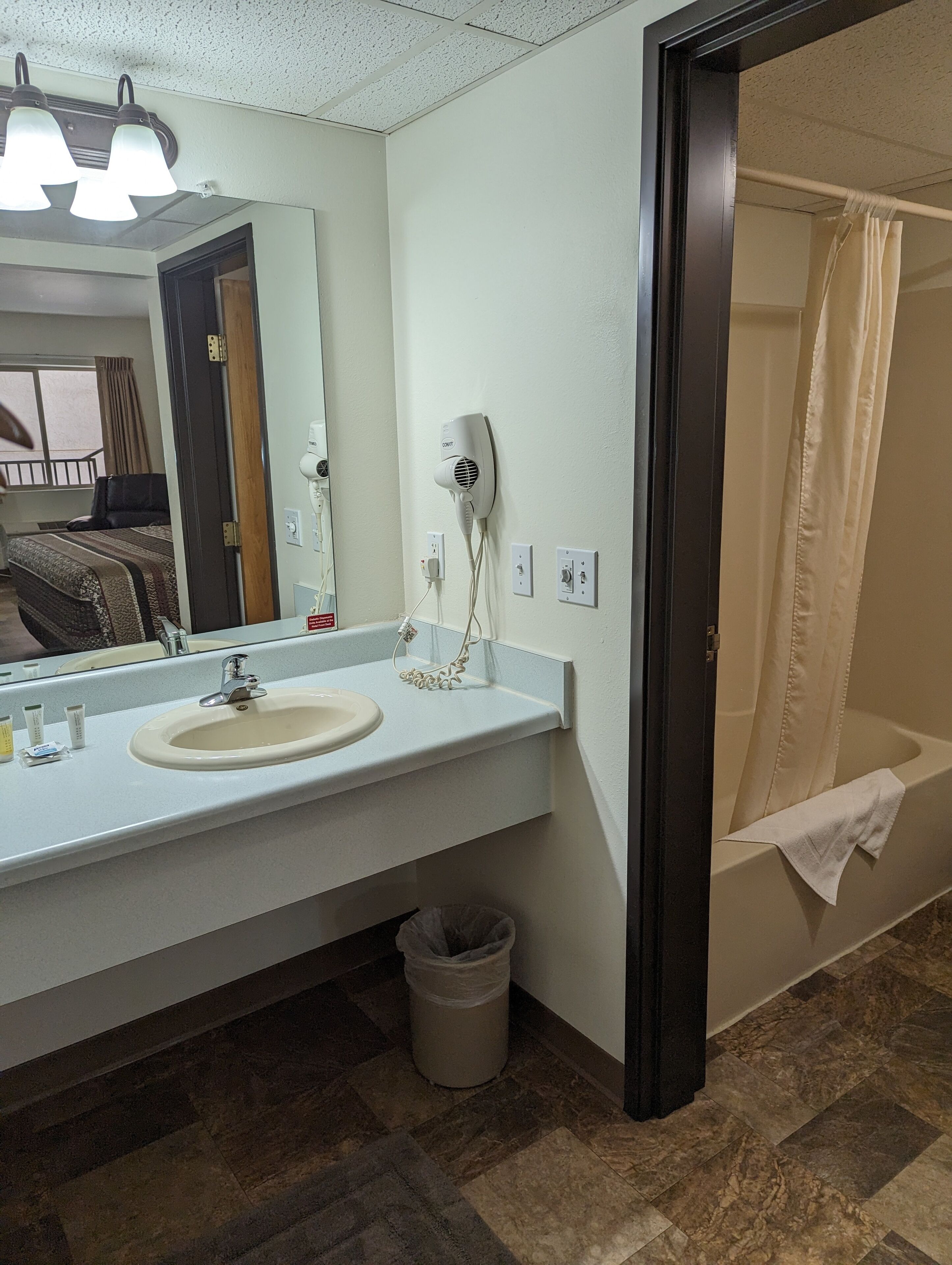 A bathroom with a sink, mirror, hairdryer, and a shower with a towel.