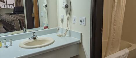 A bathroom with a sink, mirror, hairdryer, and a shower with a towel.