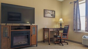 Habitación de hotel con televisión, escritorio y silla, chimenea, lámpara y ventana con cortinas.