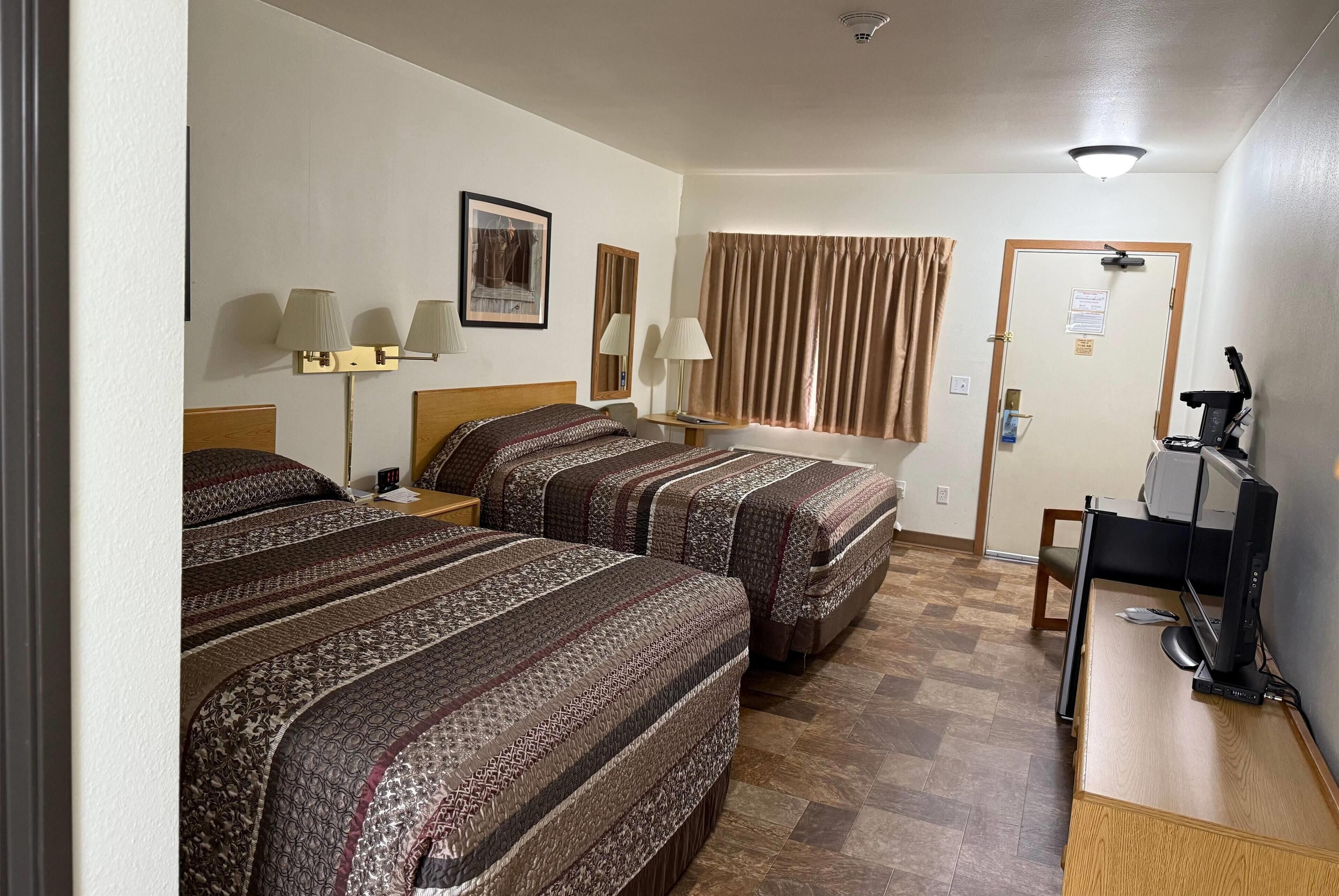 Habitación de hotel con dos camas, un escritorio con computadora, una caminadora y una ventana con cortinas.