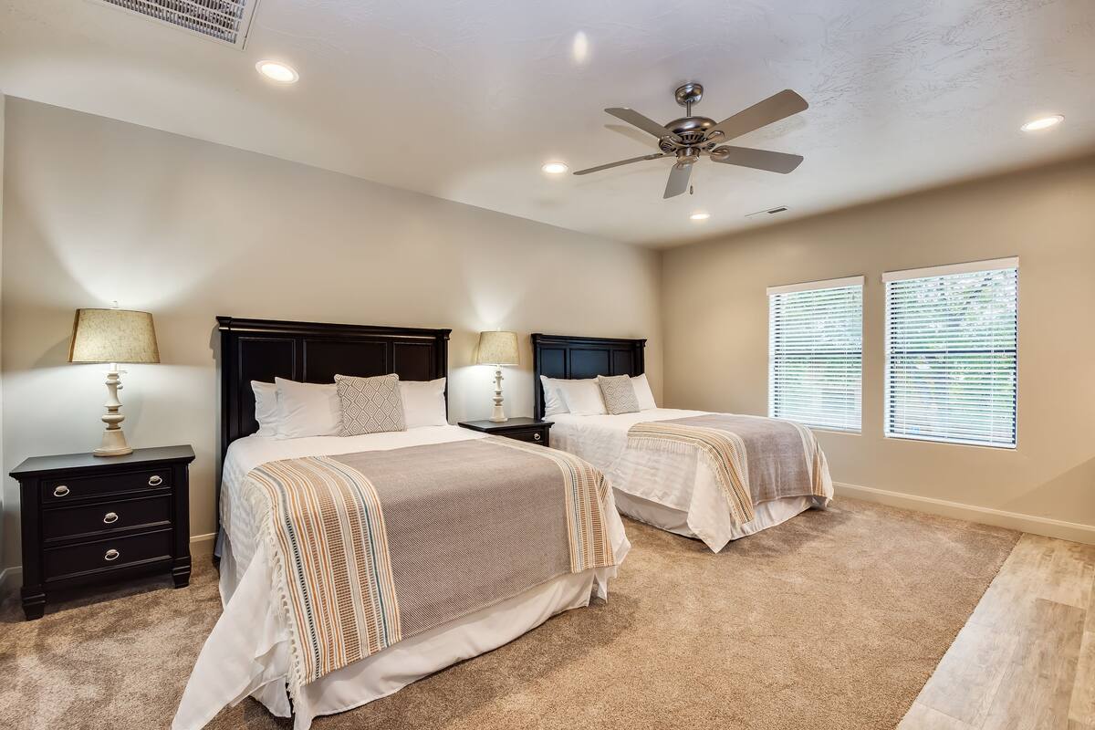 A bedroom with two beds, a ceiling fan, and a nightstand with a lamp.