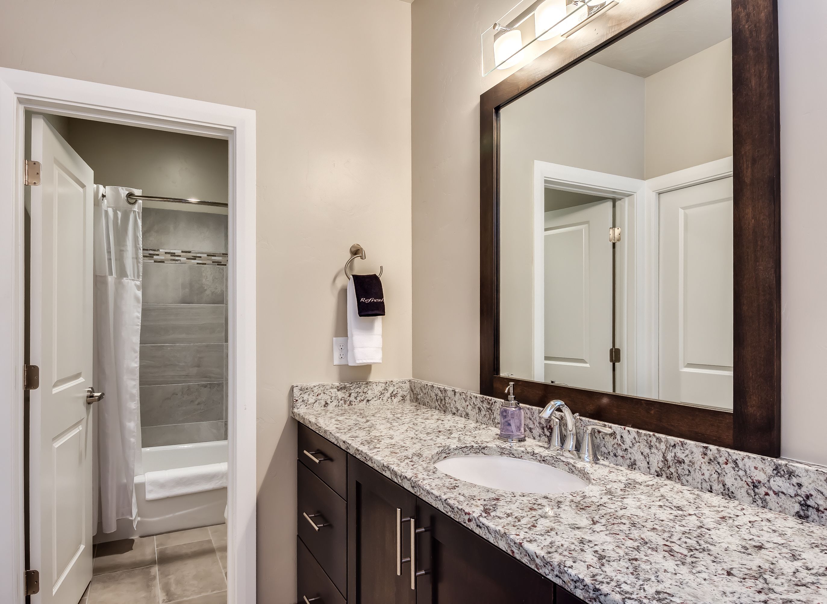 A bathroom with a marble sink, dark wooden cabinets, a large mirror, and a shower area with a glass door.