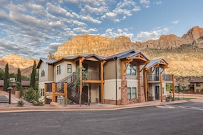 A multi-story hotel with a stone facade, wooden balconies, and a parking lot in front. - Watchman Villas (Springdale)