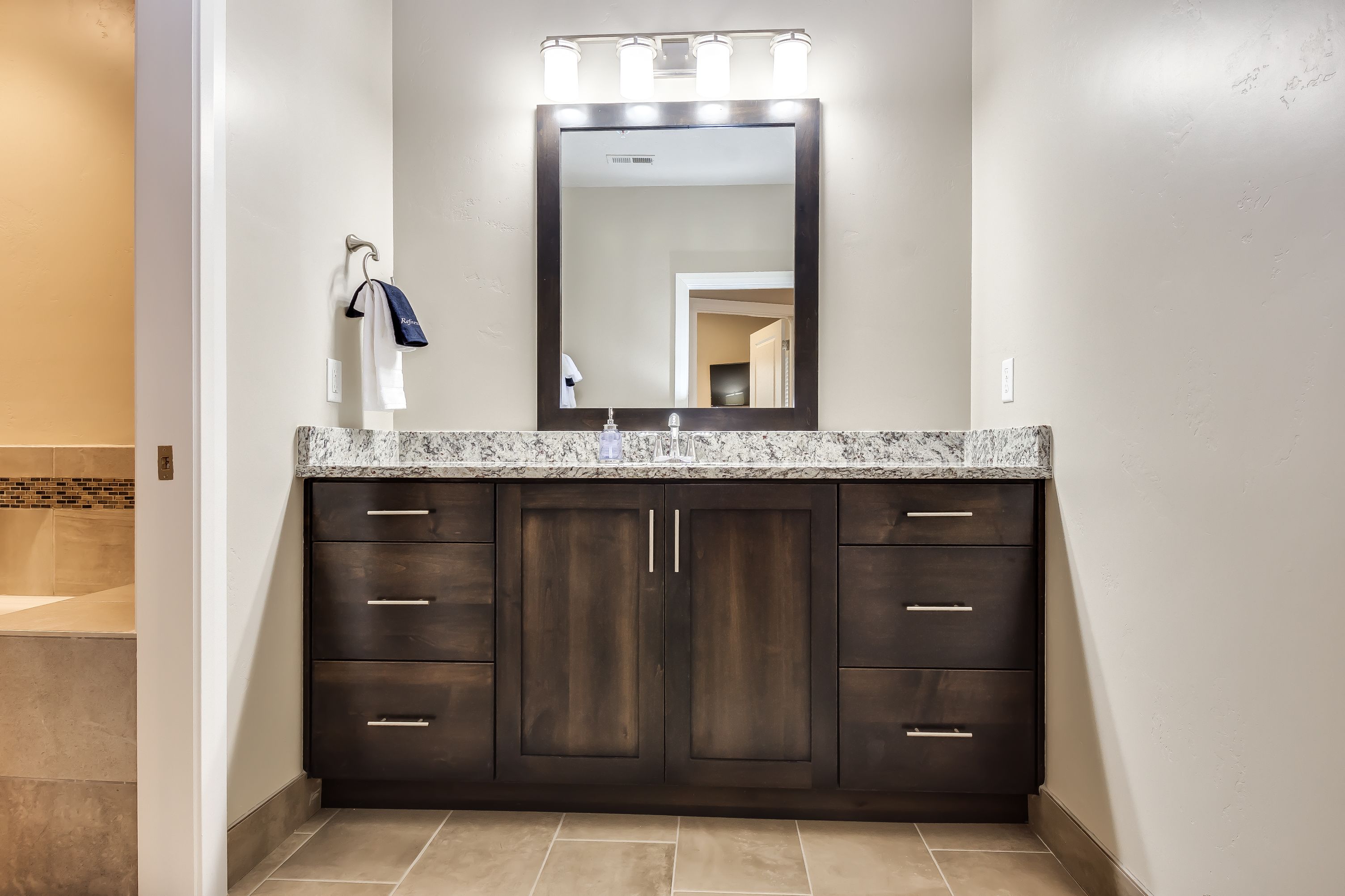 Un baño con tocador de madera oscura, encimera de granito y espejo con iluminación.