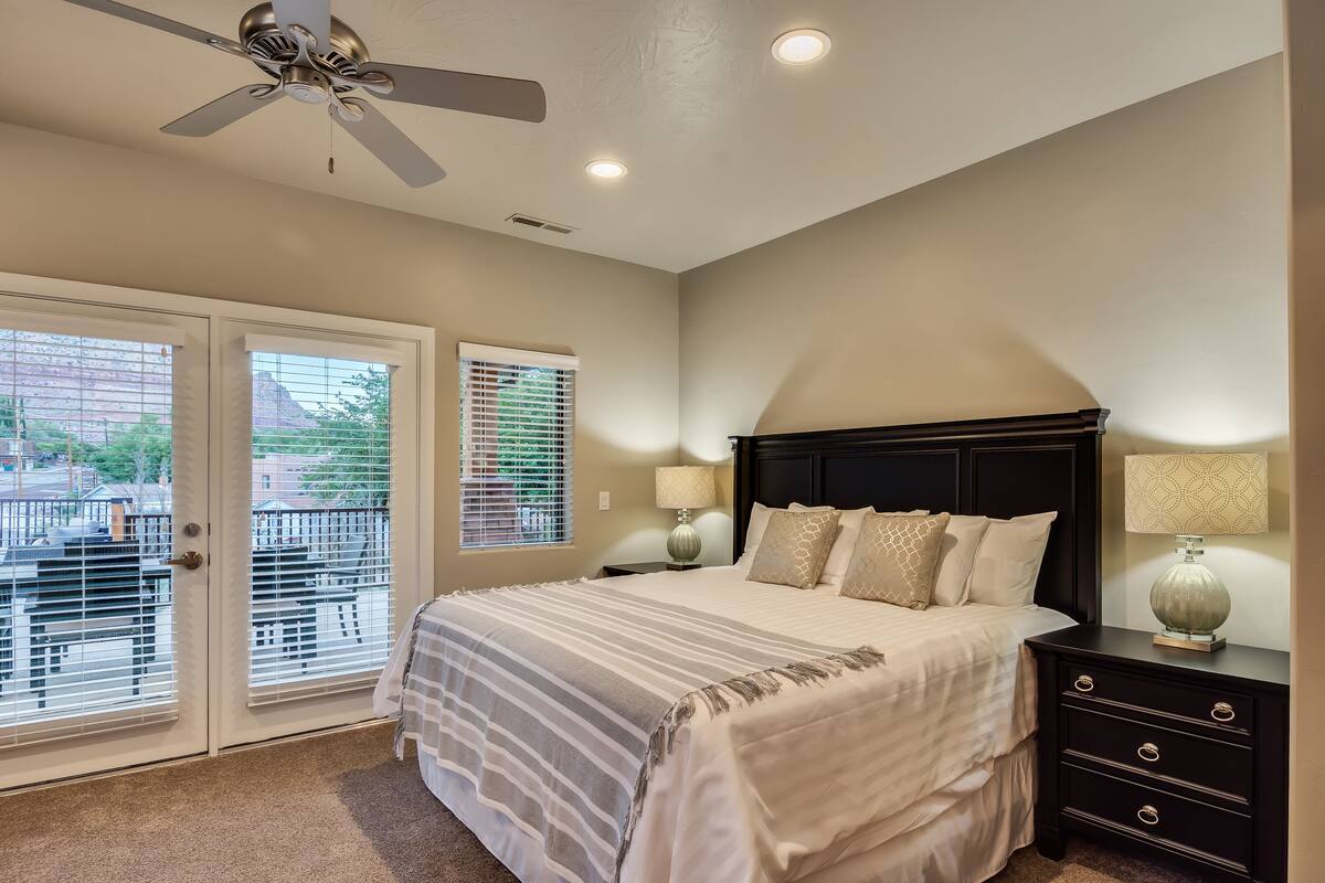 A bedroom with a bed, a nightstand, a lamp, a ceiling fan, and a view through the door.