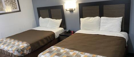 Une chambre d’hôtel avec deux lits simples, chacun recouvert d’une courtepointe marron et agrémenté d’un coussin décoratif à motifs. Une table de chevet avec une lampe se trouve entre les lits, et un tableau encadré est accroché au mur, à gauche.