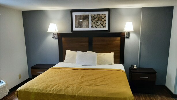 Una habitación de hotel con una cama grande, dos mesitas de noche, un cabecero con un cuadro enmarcado y dos lámparas de pared.