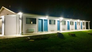 Una hilera de edificios de una sola planta con puertas azules, probablemente un motel o casa de huéspedes, con iluminación exterior en la noche.
