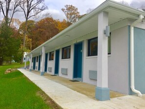 A row of motel rooms with individual doors and windows, a covered walkway, and a grassy area with trees. - Hillside Motel (Glen Mills)